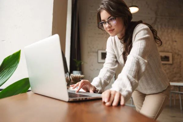 カフェで勉強しながらノートパソコンを使って眼鏡をかける若い美人白人女性の姿 — ストック写真