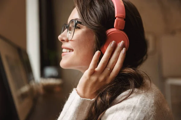 照片中年轻美丽的高加索女人戴着耳机 微笑着在咖啡馆里听音乐 — 图库照片