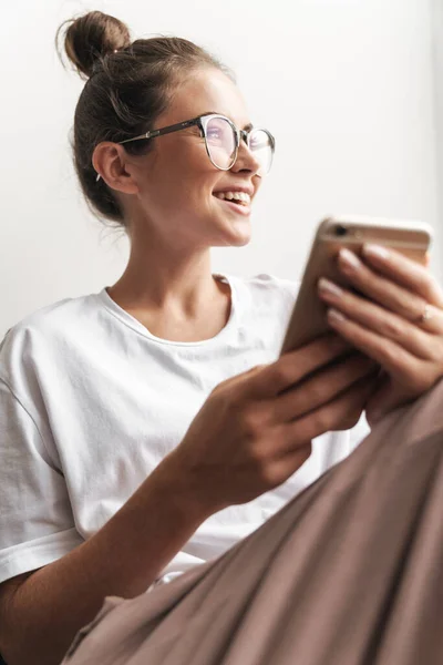 Зображення Привабливої Жінки Окулярах Посміхаючись Друкуючи Мобільному Телефоні Сидячи Дивані — стокове фото