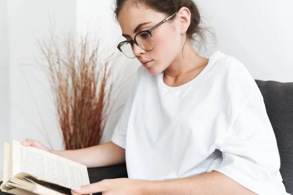 Imagem Uma Jovem Mulher Séria Óculos Lendo Livro Enquanto Senta — Fotografia de Stock