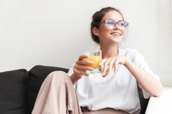 在客厅的沙发上 一个戴着眼镜的漂亮女人一边看一边喝果汁的形象 — 图库照片