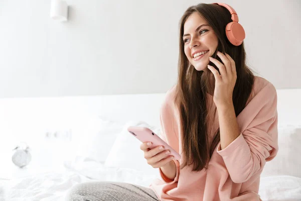 쾌활하고 스러운 소녀가 잠옷을 침실에 헤드폰을 전화를 음악을 — 스톡 사진