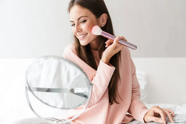 Sonriente Chica Encantadora Usando Pijamas Aplicando Maquillaje Mientras Está Sentado — Foto de Stock