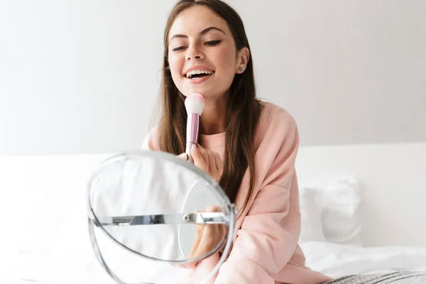 Sonriente Chica Encantadora Usando Pijamas Aplicando Maquillaje Mientras Está Sentado — Foto de Stock
