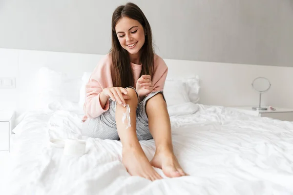 Härlig Flicka Bär Pyjamas Tillämpa Kroppslotion Medan Sitter Sängen Sovrummet — Stockfoto
