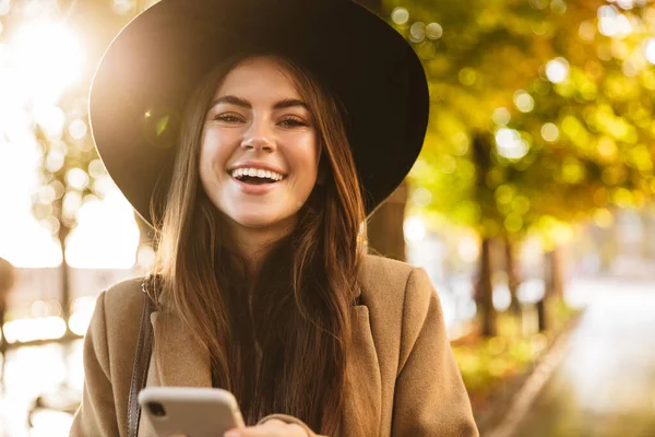 Portré Boldog Kabátot Kalapot Visel Mobiltelefon Miközben Sétál Őszi Parkban — Stock Fotó