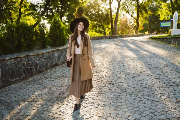 照片中 穿着秋衣 头戴礼帽的女人在户外绿地公园散步时面带微笑 — 图库照片