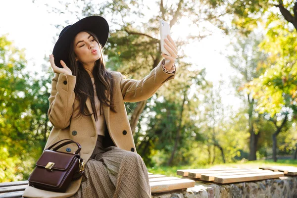 Imagem Mulher Elegante Casaco Outono Chapéu Usando Smartphone Enquanto Sentado — Fotografia de Stock