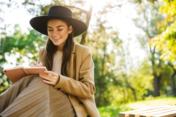 公園のベンチに座っている間 秋のコートや帽子を保持日記本で楽しい女性のイメージ — ストック写真