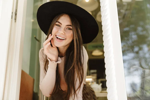 Imagen Joven Morena Sombrero Sonriendo Mientras Mira Fuera Ventana Abierta —  Fotos de Stock