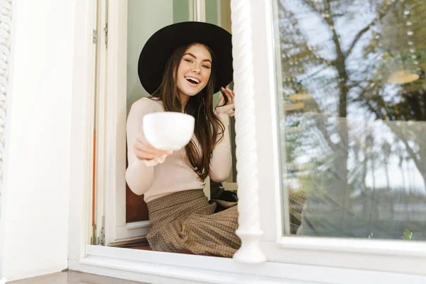 Imagem Mulher Alegre Chapéu Sorrindo Enquanto Bebe Xícara Chá Sentado — Fotografia de Stock