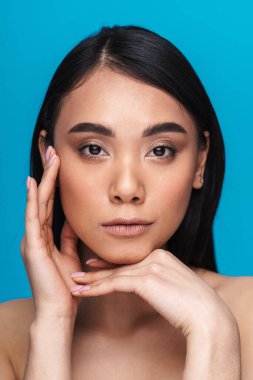 Mavi duvar arkasında yalnız poz veren güzel, memnun, pozitif Asyalı genç bir kadının görüntüsü.