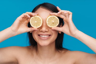 Asyalı neşeli, iyimser, güzel bir kadının mavi duvar arkasında limon kaplı gözlerle poz verdiği bir fotoğraf..