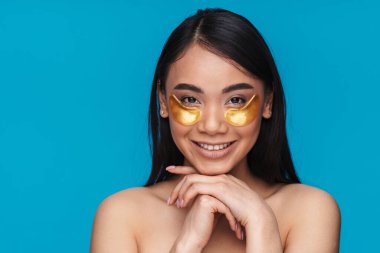 Asyalı mutlu iyimser kadının mavi duvar arkasında poz verdiği fotoğraf. Yamalı göz altı derisine dikkat et..