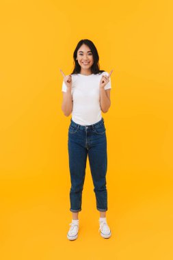 Sarı arka planda izole edilmiş, telif boşluğunu gösteren ve gülümseyen Asyalı genç esmer kadının tam boy görüntüsü.