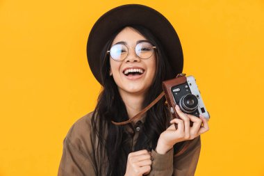 Sarı arka planda izole edilmiş retro kamera kullanan Asyalı genç esmer kadın görüntüsü