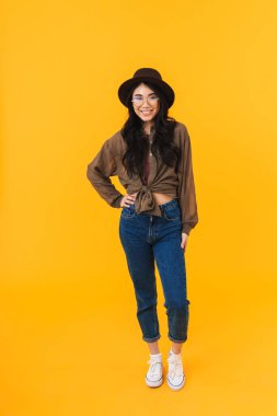 Sarı arka planda izole edilmiş, gülümseyen ve kameraya poz veren Asyalı esmer bir kadının tam boy görüntüsü.
