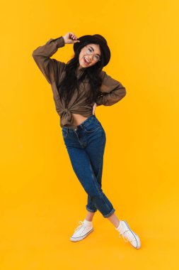 Sarı arka planda izole edilmiş, gülümseyen ve kameraya poz veren Asyalı esmer bir kadının tam boy görüntüsü.