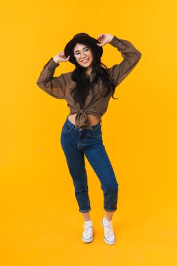 Sarı arka planda izole edilmiş, gülümseyen ve kameraya poz veren Asyalı esmer bir kadının tam boy görüntüsü.