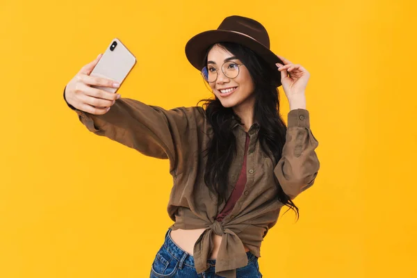 모자와 안경을 노란색 배경으로 고립된 휴대폰상에서 사진을 여자의 — 스톡 사진