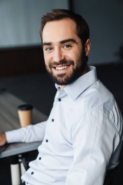 Ofiste çalışırken gülümseyen ve kahve içen beyaz gömlekli yakışıklı iş adamının portresi.