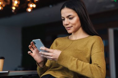 Ofiste çalışırken cep telefonu kullanan esmer, beyaz iş kadını görüntüsü