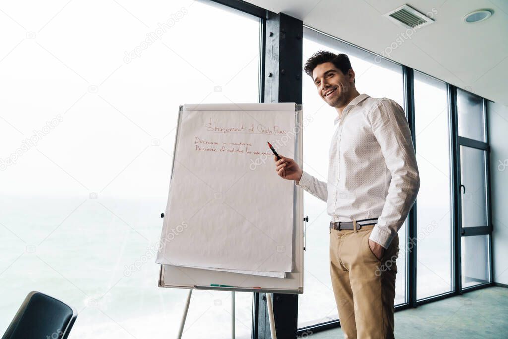 Portrait of handsome young businessman wearing white shirt standing by flipchart while working in office
