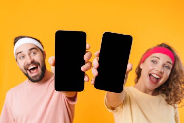 Sarı arka planda izole edilmiş, gülümseyen ve cep telefonu kullanan atletik genç çiftin portresi.