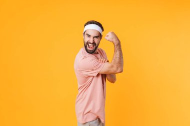 Tişörtlü, kaslı ve atletik bir genç adamın sarı arka planda izole edilmiş pazılarını göstermesi.