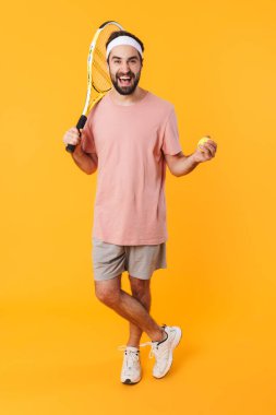 Sarı arka planda tenis oynarken tişörtlü, kaslı genç bir adamın raket tutuşu.