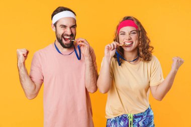 Sarı arka planda izole edilmiş ödül madalyalarıyla zaferi kutlayan saç bandı takan genç sporcu çiftin portresi.