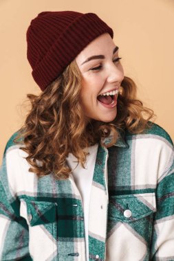 Örgü şapkalı neşeli bir kadının bej arka planda izole edilmiş bir şekilde gülüşü ve bakışları.