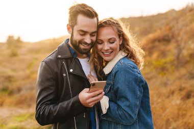 Güzel, genç, mutlu, şık bir çift. Plajda durmuş, cep telefonu kullanıyorlar.