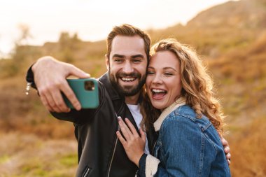 Güzel, genç, mutlu, şık bir çift plajda dikilip selfie çekiyorlar.