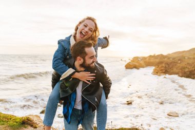 Deniz kenarında yürürken gülümseyen ve sırtına binen güzel beyaz bir çift.