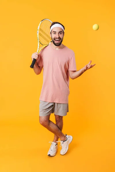 黄色の背景の上に隔離されたテニスをプレイしながらTシャツを保持ラケットで筋肉運動の若い男のイメージ — ストック写真