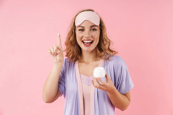 ピンクの背景に孤立した顔クリームを適用しながら スリープマスク笑顔で白人陽気な女性のイメージ — ストック写真