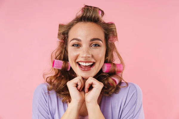 若いです幸せな女性でCurlers笑顔と見てカメラで隔離されたピンクの背景 — ストック写真