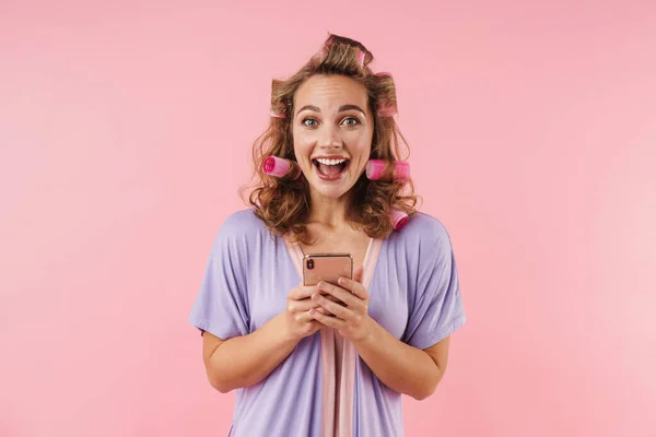 Изображение Молодой Счастливой Женщины Бигуди Улыбающейся Использующей Мобильный Телефон Розовом — стоковое фото