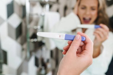 Banyoda duş aldıktan sonra hamilelik testi yapan beyaz sabahlıklı güzel sarışın bir kadın.