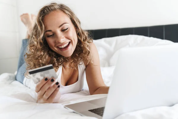 침대에 노트북 컴퓨터를 사용하여 카드를 금발의 아름다운 — 스톡 사진
