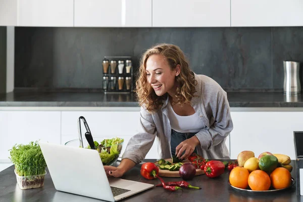 Щаслива Молода Жінка Робить Салат Кухні Рубає Овочі Дивлячись Ноутбук — стокове фото
