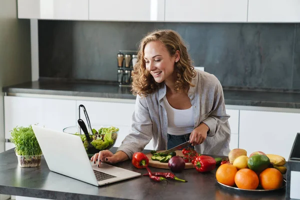 Счастливая Молодая Женщина Делает Салат Кухне Режет Овощи Смотрит Ноутбук — стоковое фото