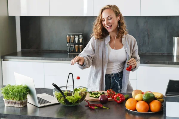 Щаслива Молода Жінка Робить Салат Кухні Рубає Овочі Дивиться Ноутбук — стокове фото