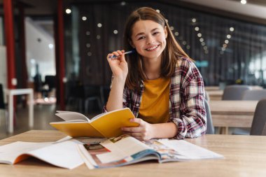 Kolej kütüphanesinde okurken ödevlerini yaparken gülümseyen beyaz kız görüntüsü