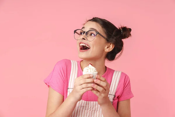 照片上的兴奋迷人的女孩 戴着眼镜 手里拿着蛋糕 在粉色的背景下孤独地表达着惊奇 — 图库照片