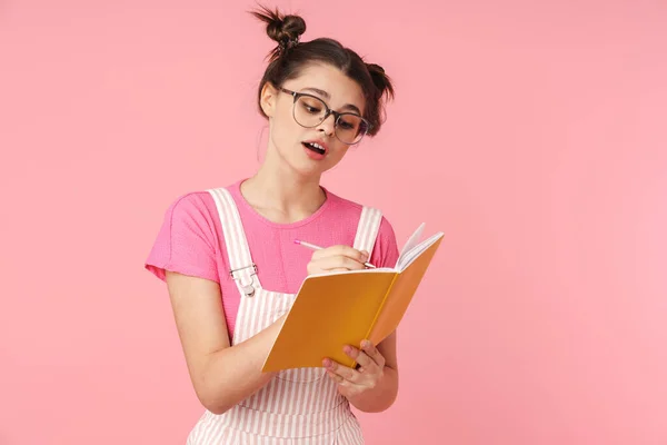 Foto Van Serieus Charmant Meisje Bril Schrijven Oefenboek Geïsoleerd Roze — Stockfoto