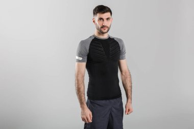 Gri arka planda izole edilmiş, spor giyimli, poz veren ve kameraya bakan genç güçlü bir adamın görüntüsü