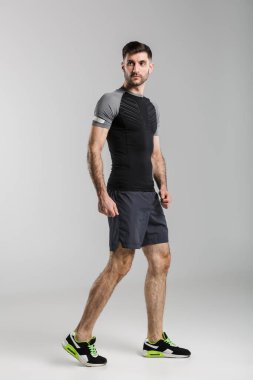 Gri arka planda yalnız başına poz veren ve bakan traşsız genç bir adam.