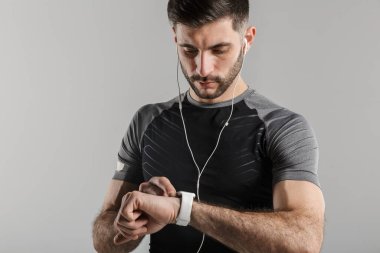 Gri arka planda izole edilmiş akıllı kaset ve kulaklık kullanan traşsız genç sporcunun görüntüsü